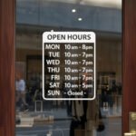 Custom open hours decal applied on wooden glass door, business storefront vinyl lettering, personalized store hours sticker by TheRetractableBanner.Shop